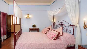 Ein Himmelbett mit Baldachin, ein Nachttisch mit Lampe und ein Beistelltisch mit Kerze.