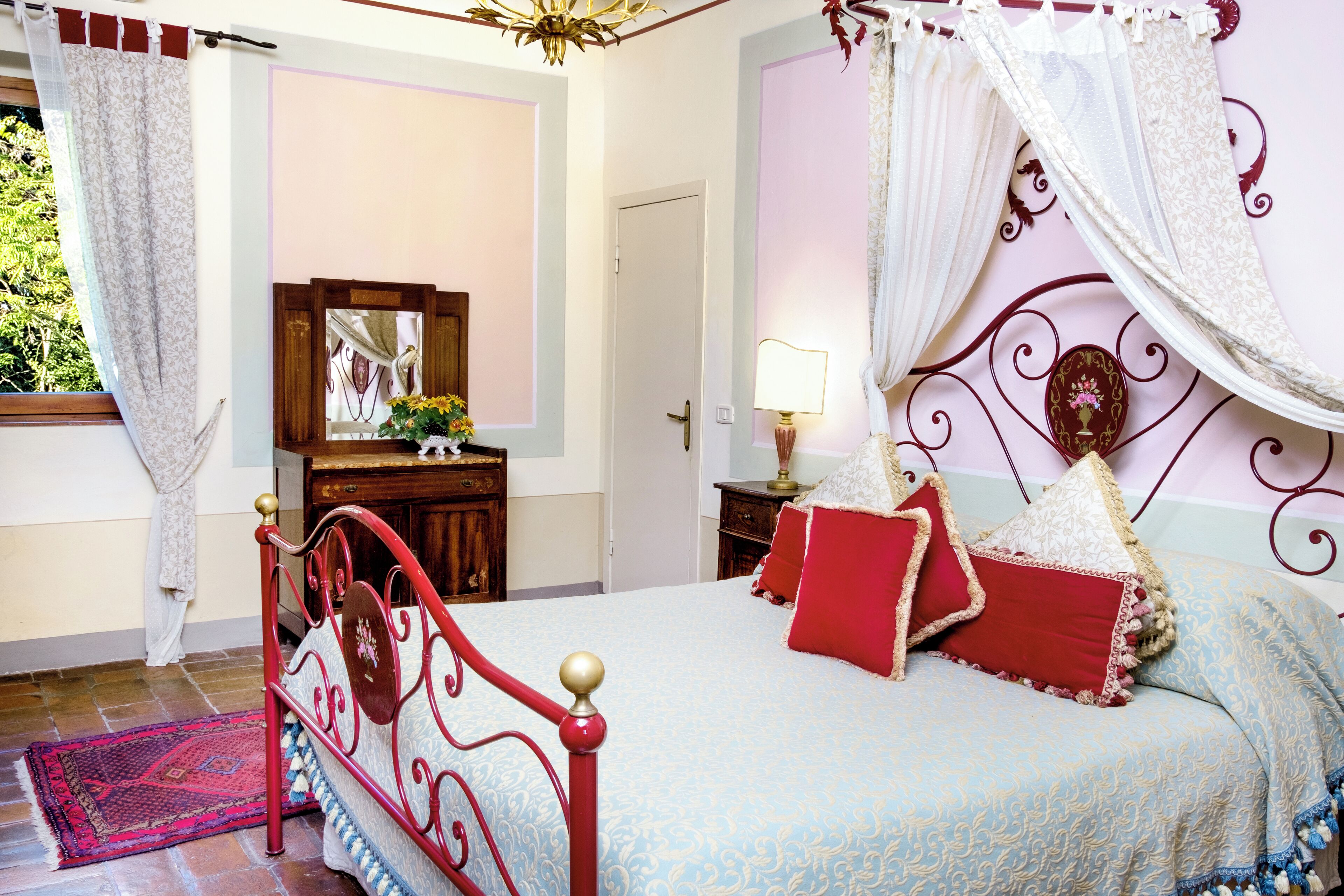 Een slaapkamer met een hemelbed, een houten dressoir en een spiegel.