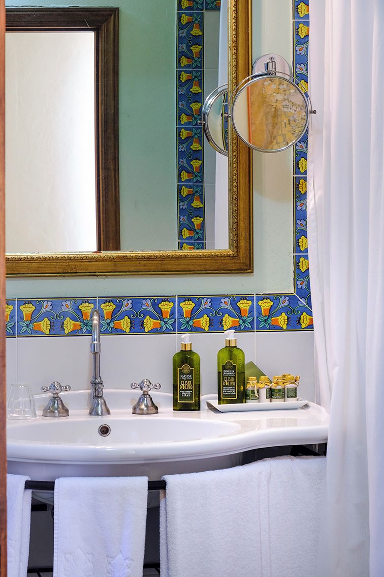 A bathroom with a white sink, two faucets, a mirror with a gold frame, and a decorative tile backsplash.