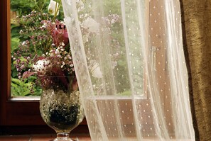 A window with a lace curtain and a vase of flowers on a wooden surface. - Locanda del Molino (Cortona)