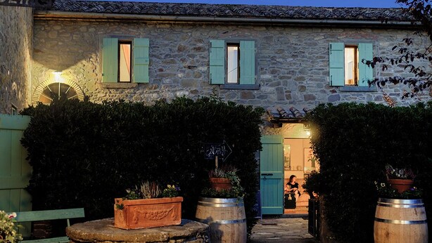 Un edificio de piedra con encanto rústico, que presenta una entrada acogedora y un pequeño espacio al aire libre para sentarse.