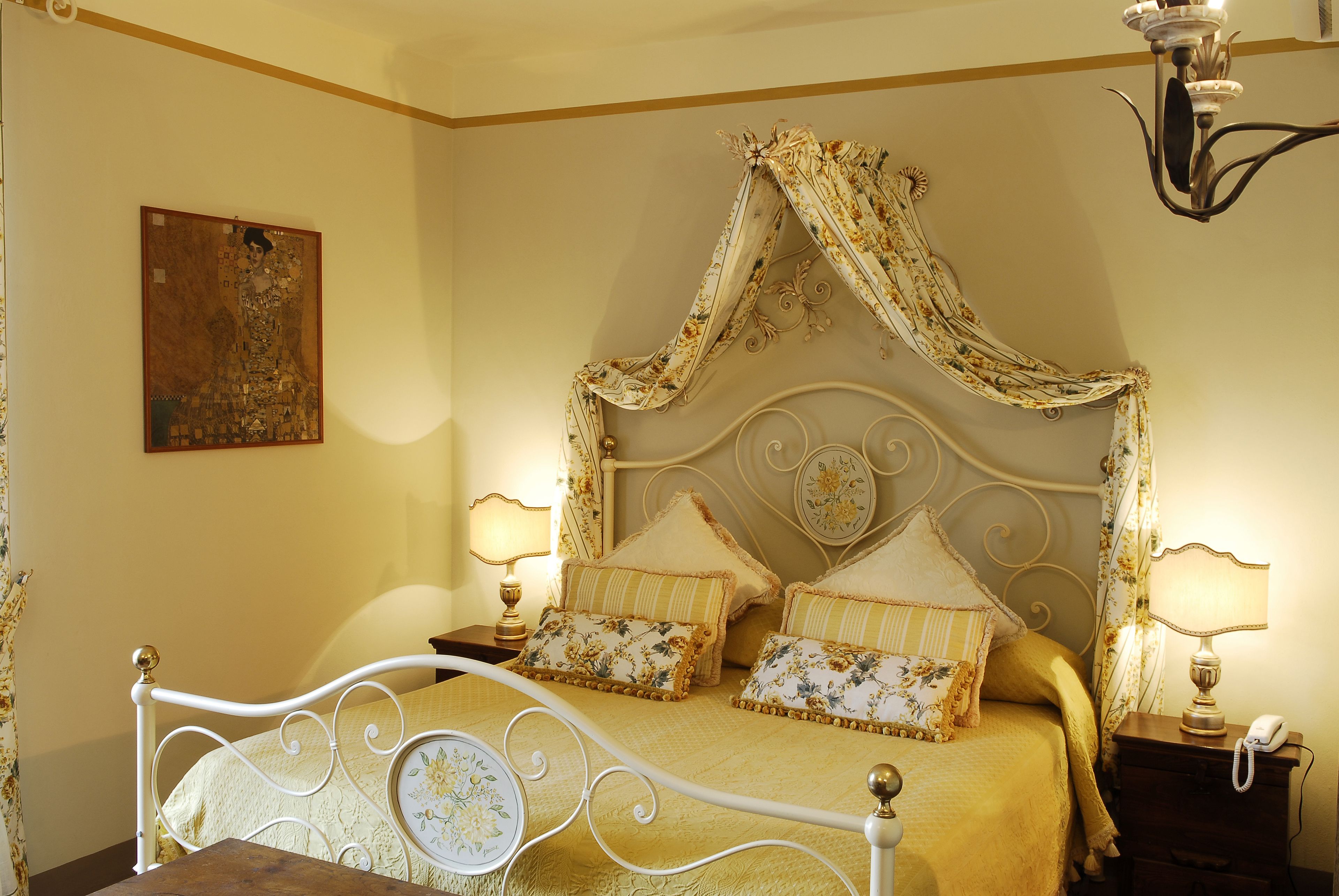 A bed with a canopy, two bedside tables with lamps, and a painting on the wall.
