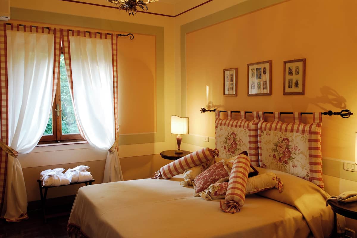 A neatly made bed with striped pillows, a bedside table with a lamp, and a window with curtains.