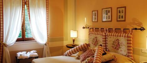 A neatly made bed with striped pillows, a bedside table with a lamp, and a window with curtains.