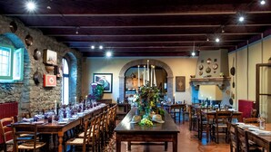 Un restaurante con una larga mesa compartida, sillas de madera, paredes de piedra y diversos utensilios de cocina exhibidos en las paredes.