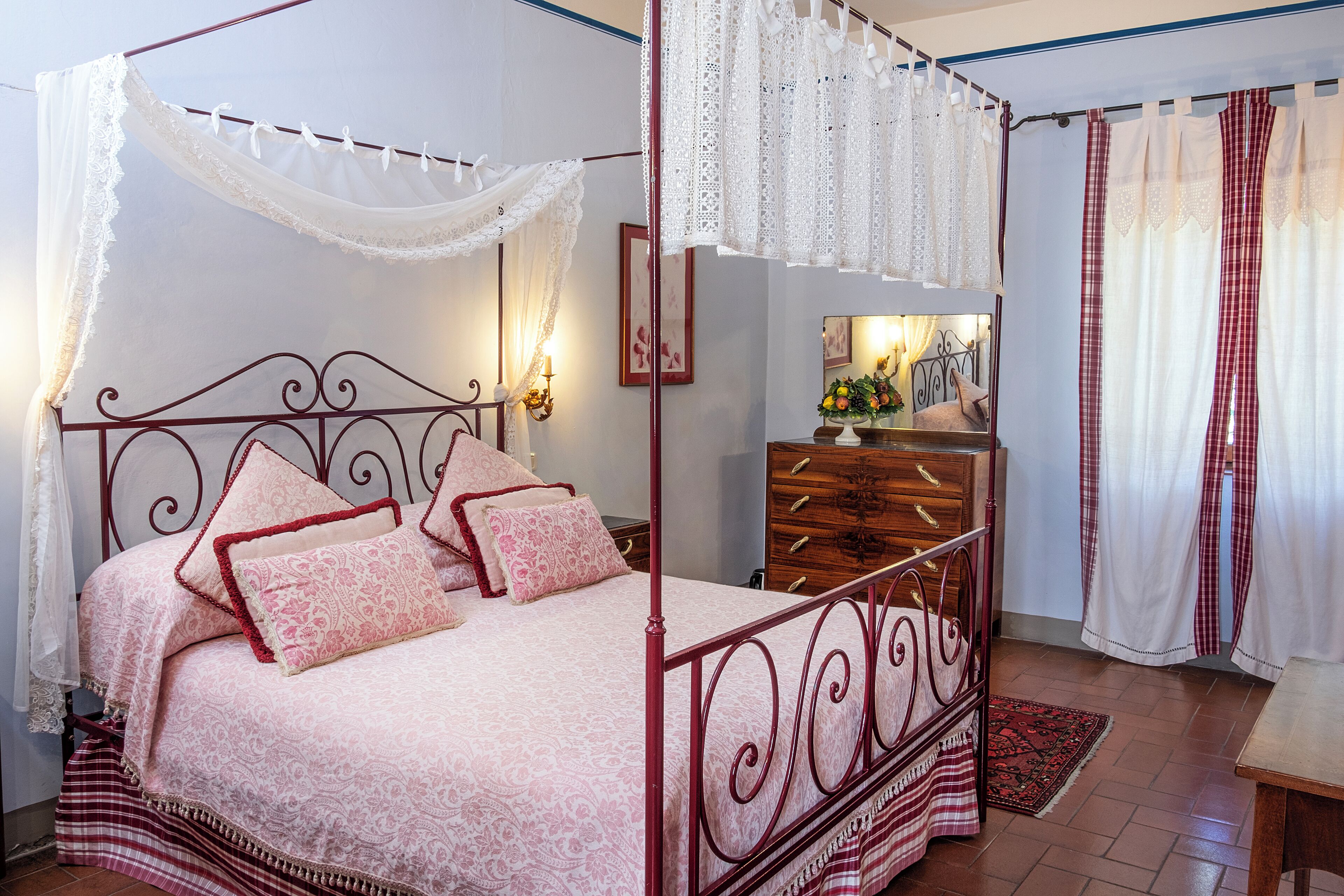Ein Himmelsbett mit rotem Metallgestell, weißem Baldachin und einer zudeckenden Bettdecke mit Blumenmuster.