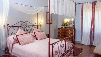 Ein Himmelsbett mit rotem Metallgestell, weißem Baldachin und einer zudeckenden Bettdecke mit Blumenmuster.