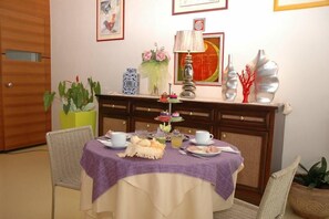 A dining area with a table set for two, a lamp, decorative vases, and a fruit bowl. - Hotel Elvia (Lignano Sabbiadoro)