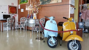 A room with a dining table, chairs, a chandelier, and vintage scooters.