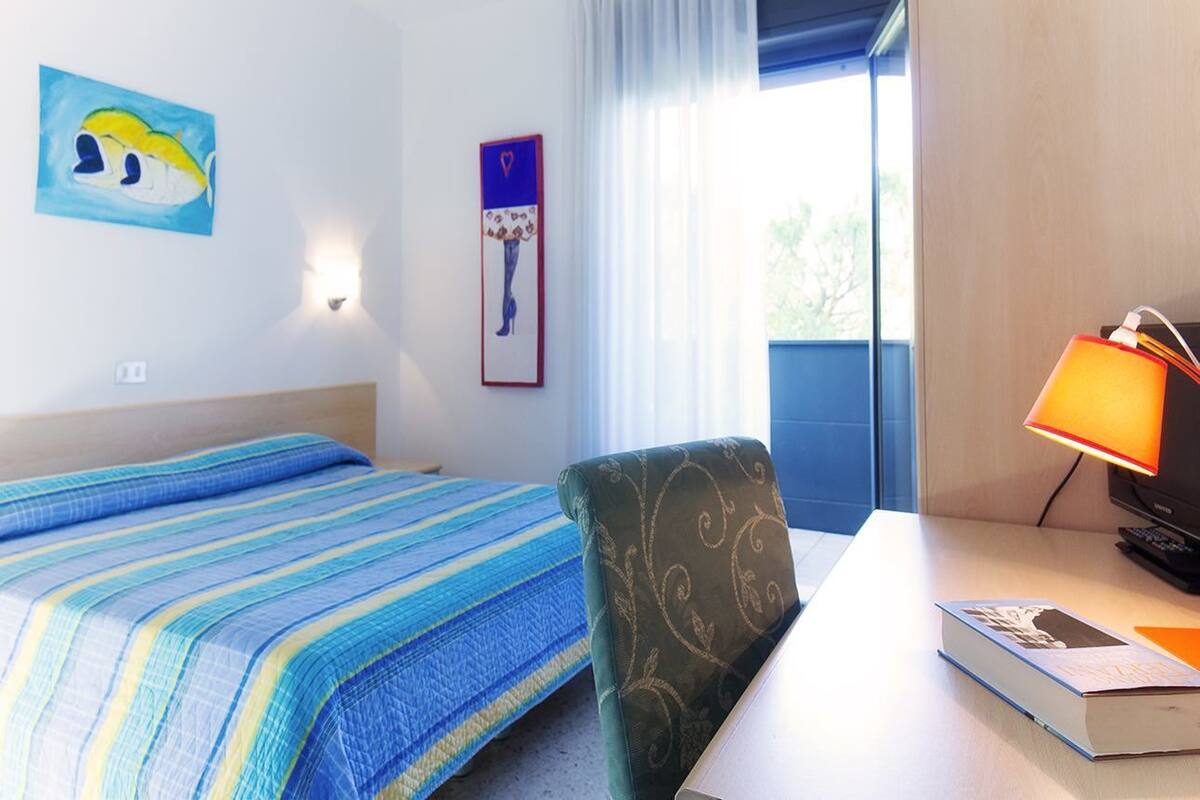 Een hotelkamer met een bed, een stoel, een bureau met een lamp en een schilderij aan de muur.