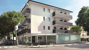 A modern hotel with a flat roof, multiple balconies, and a covered entrance area.