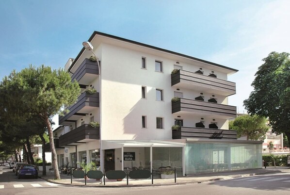 A modern hotel with a flat roof, multiple balconies, and a covered entrance area. - Hotel Elvia (Lignano Sabbiadoro)