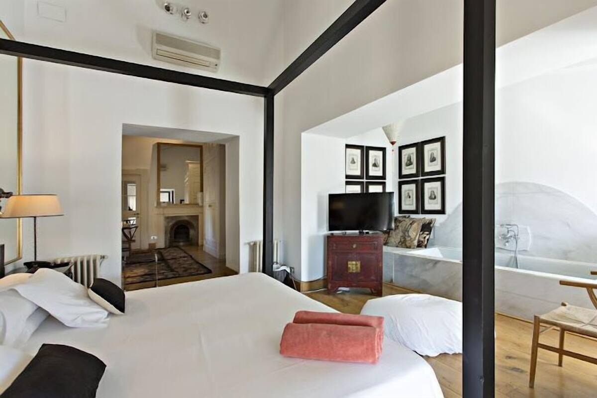 A hotel room with a large bed, a television, a fireplace, and a view of the outside.