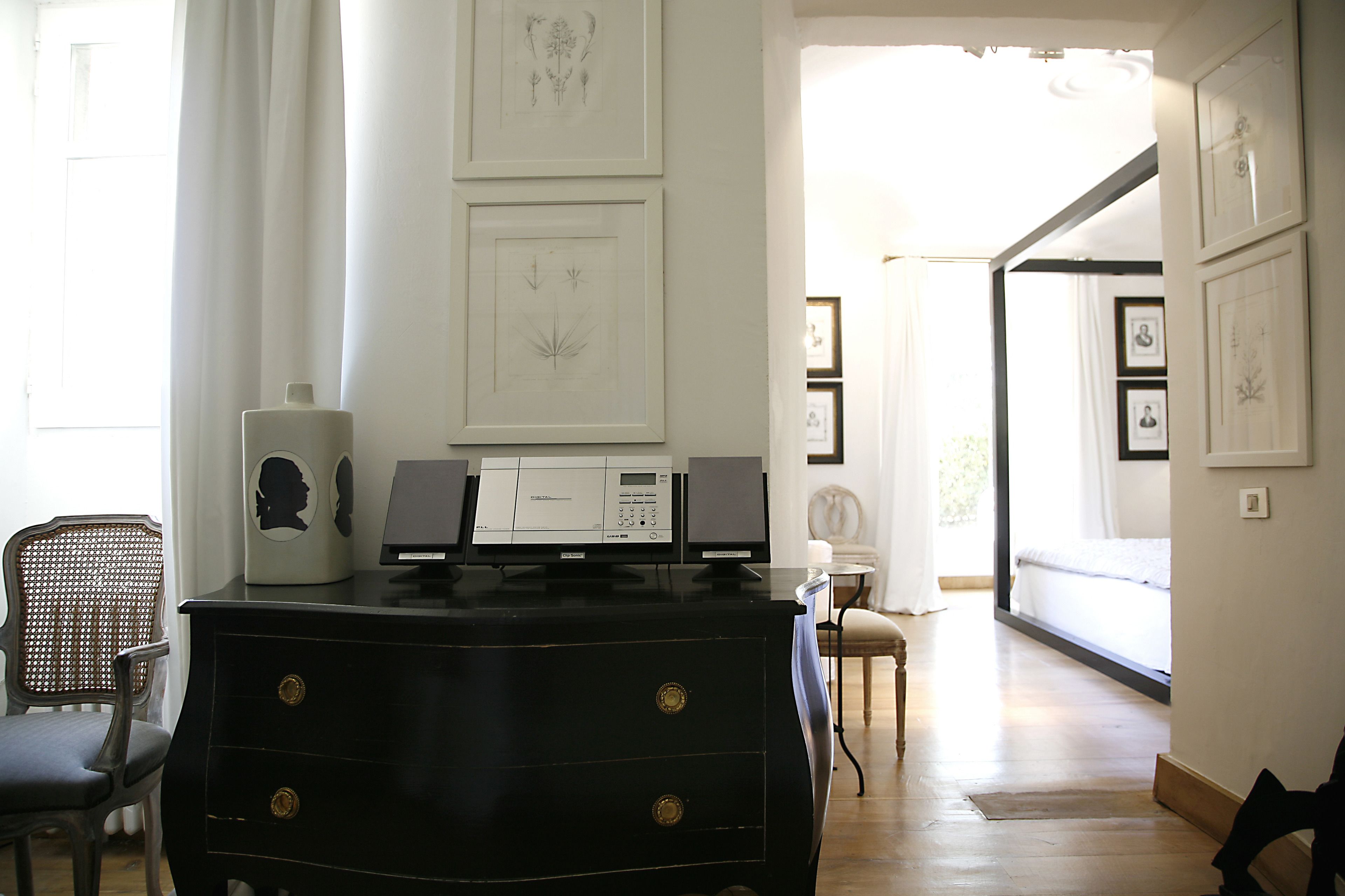 Een kamer met een zwarte kast met lades, een witte stoel en ingelijste botanische prints aan de wand.