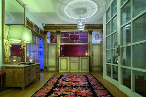Une pièce avec une commode en bois, un miroir, un lustre et une moquette à motifs floraux.
