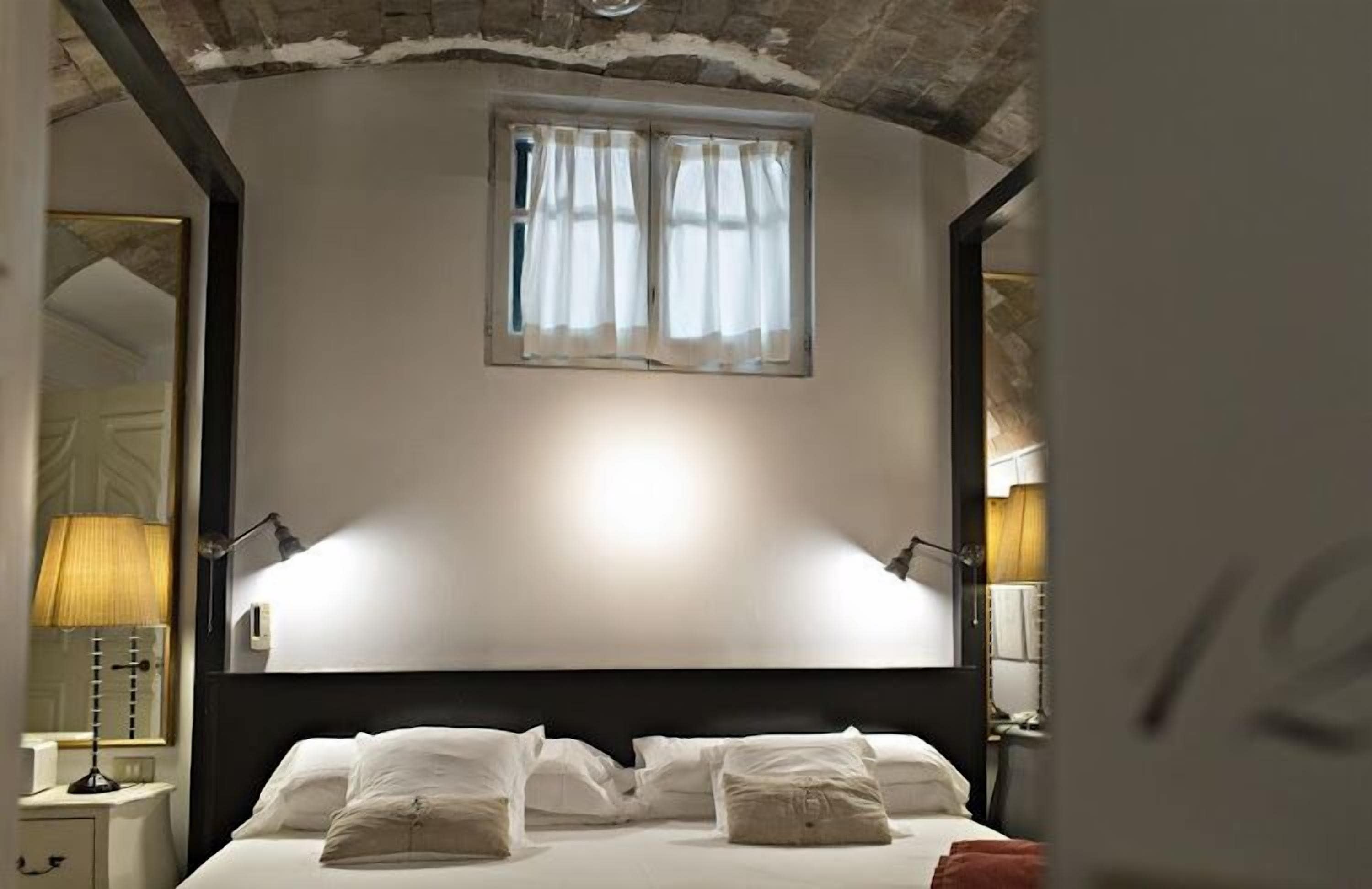 Una camera da letto con un letto grande, una finestra con tende, un comodino con una lampada e uno specchio.