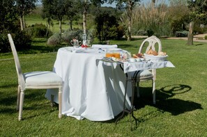 Un espace de restauration en plein air avec une table dressée pour deux personnes, entourée d’une végétation luxuriante et d’arbres.