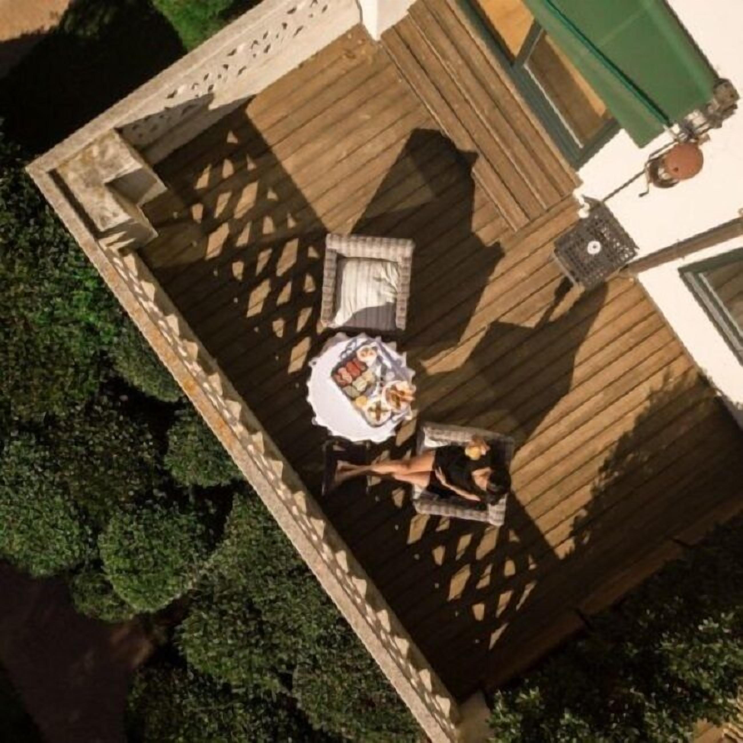 Vista aérea de una terraza de madera con una mesa y sillas, rodeada de follaje.