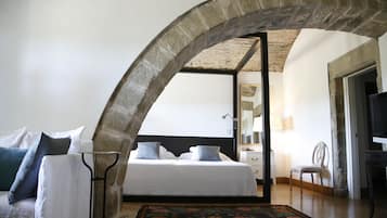 Un dormitorio con una cama grande, un arco de piedra, suelo de madera y una mesita de noche con lámpara.