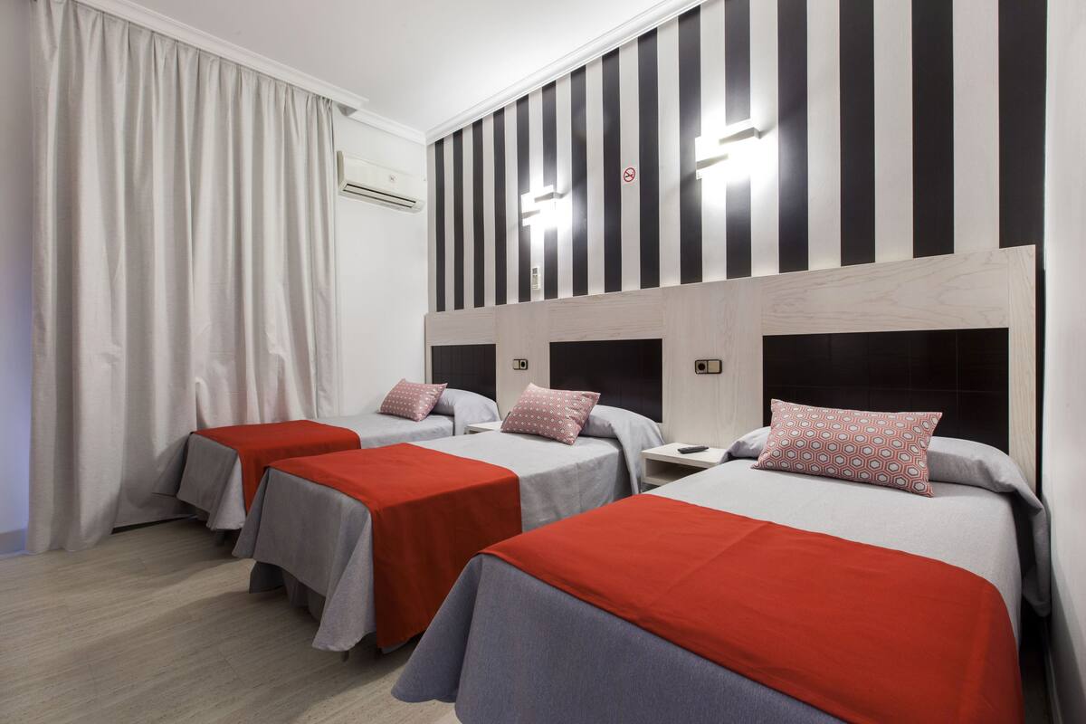 A hotel room with three beds, each with a red and grey bedspread, and a striped wall design.