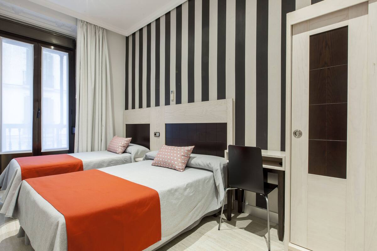 A hotel room with two beds, a desk, and a wardrobe.
