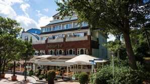 Un hotel de estilo arquitectónico europeo tradicional, con una entrada destacada que incluye un porche cubierto y macetas con plantas.