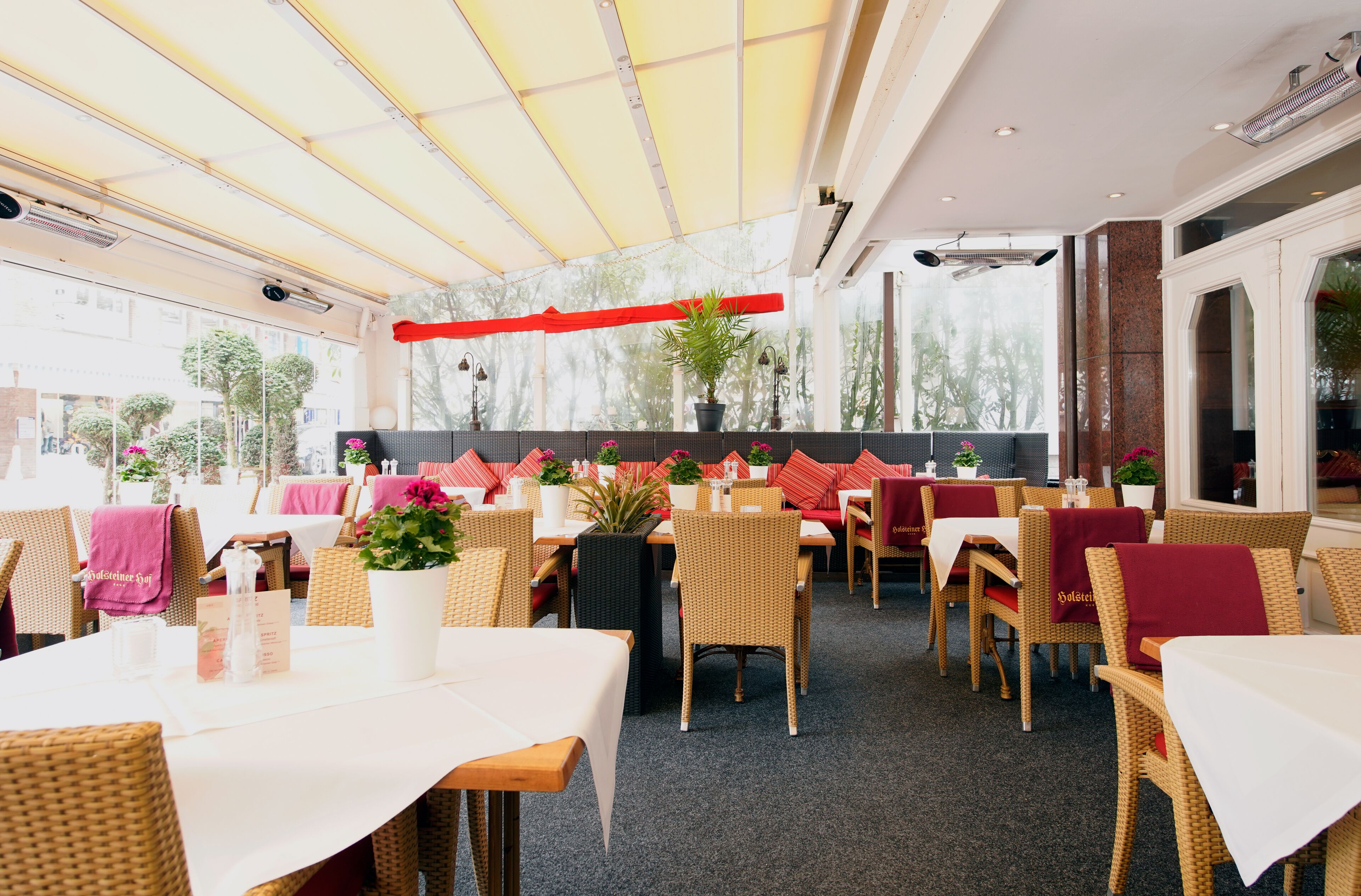 Ein Restaurant mit Korbmöbeln, roten Kissen und Topfpflanzen.