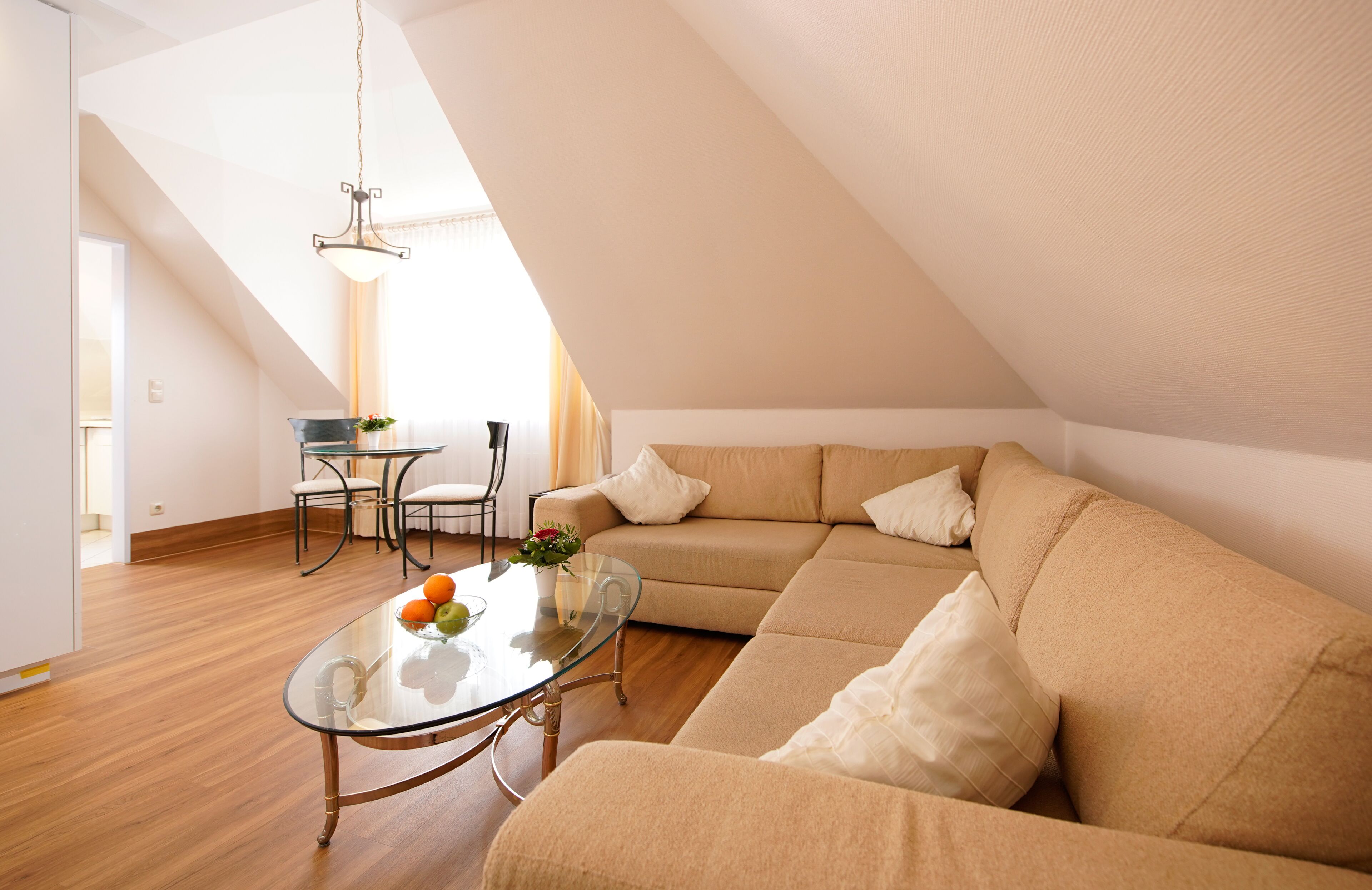 A modern living room with a glass coffee table, beige sofa, and a dining area with chairs and a table.