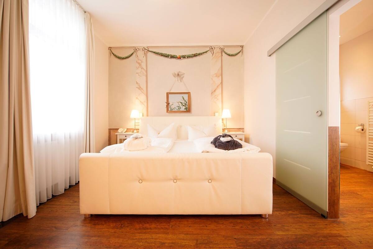 A hotel room with a large bed, two bedside tables, a nightstand, a framed picture on the wall, and a sliding door to the bathroom.
