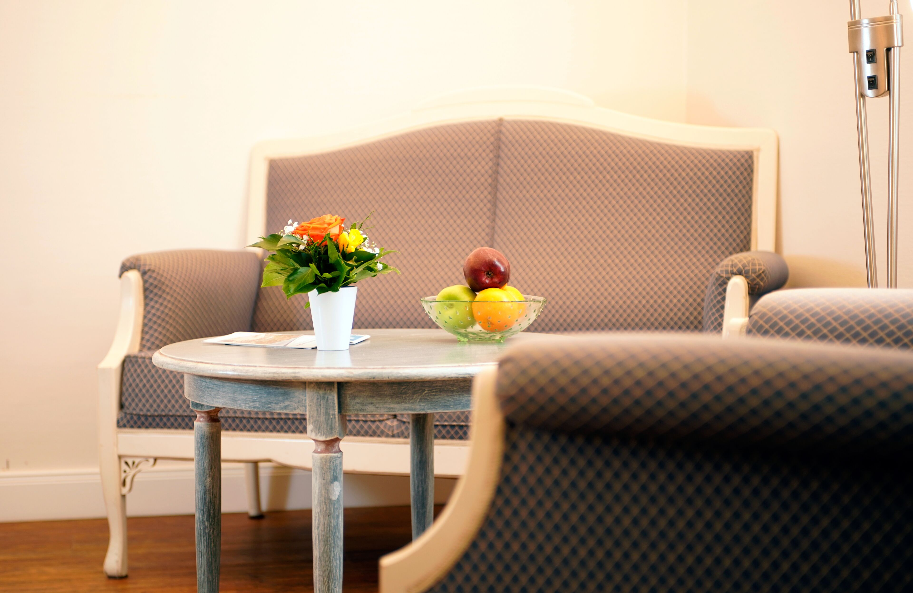 Un coin repas avec une table ronde, un vase de fleurs et un saladier de fruits.