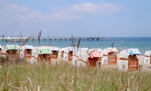 Cabañas de playa con toldos a rayas, un muelle al fondo y un primer plano con césped.