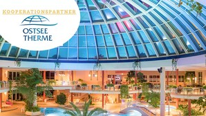 Piscina interior moderna con techo de cristal, rodeada de áreas de descanso y plantas de interior.