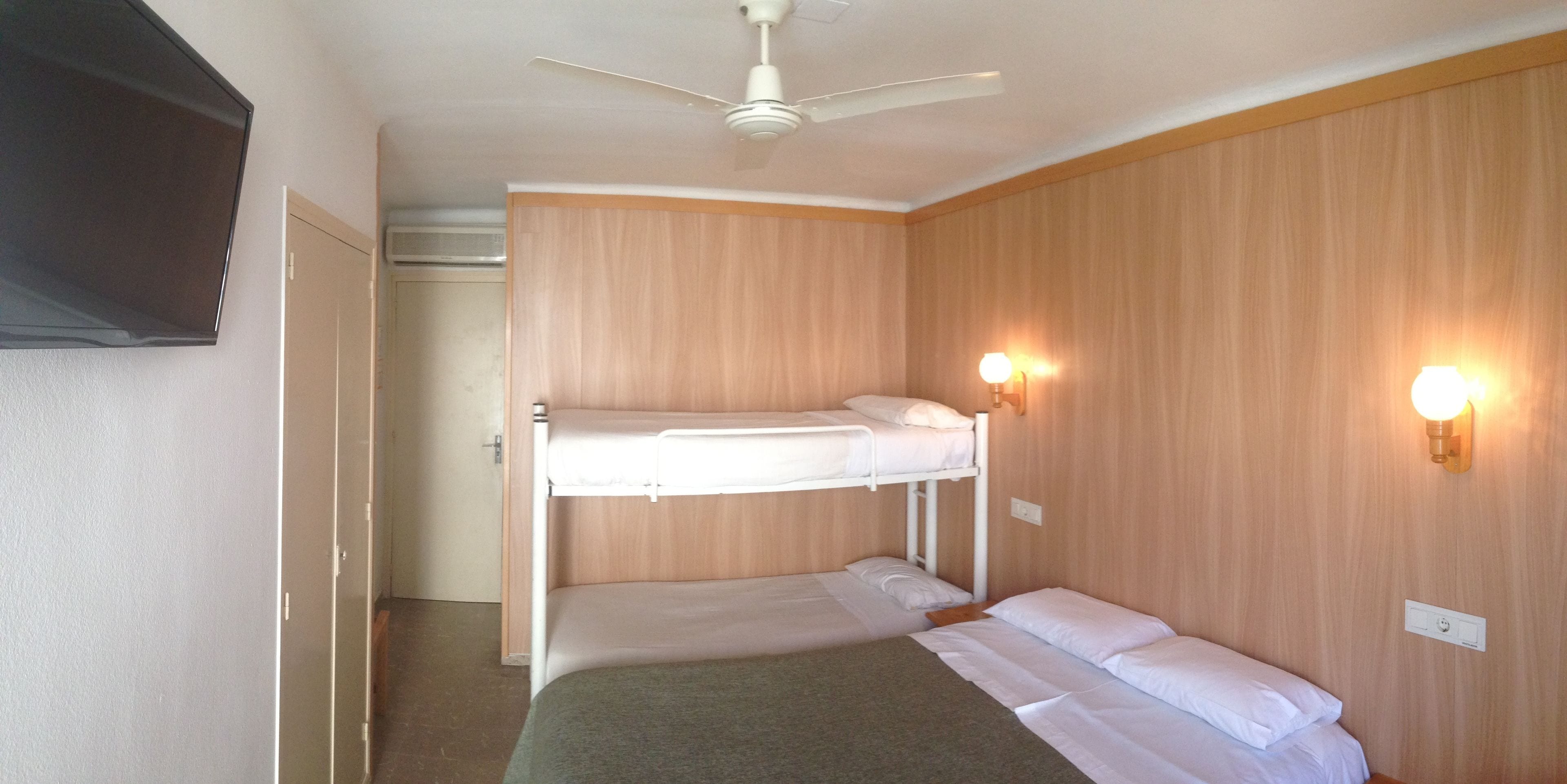 Une chambre avec des lits superposés, un ventilateur de plafond et des lampes fixées au mur.