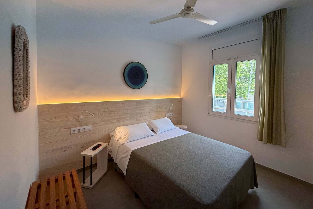 Une chambre à coucher comprenant un lit, un ventilateur de plafond, une table de chevet, une commode, une fenêtre avec des rideaux et une assiette décorative fixée au mur.