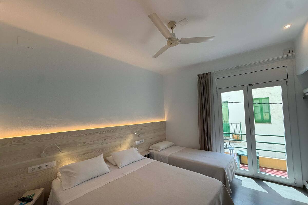 Une chambre d’hôtel avec deux lits, un ventilateur de plafond, une fenêtre donnant sur un balcon et une porte menant à l’extérieur.