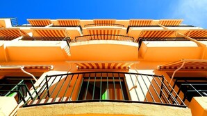 Un immeuble à plusieurs étages doté de balcons, chacun surmonté d’un auvent à rayures.