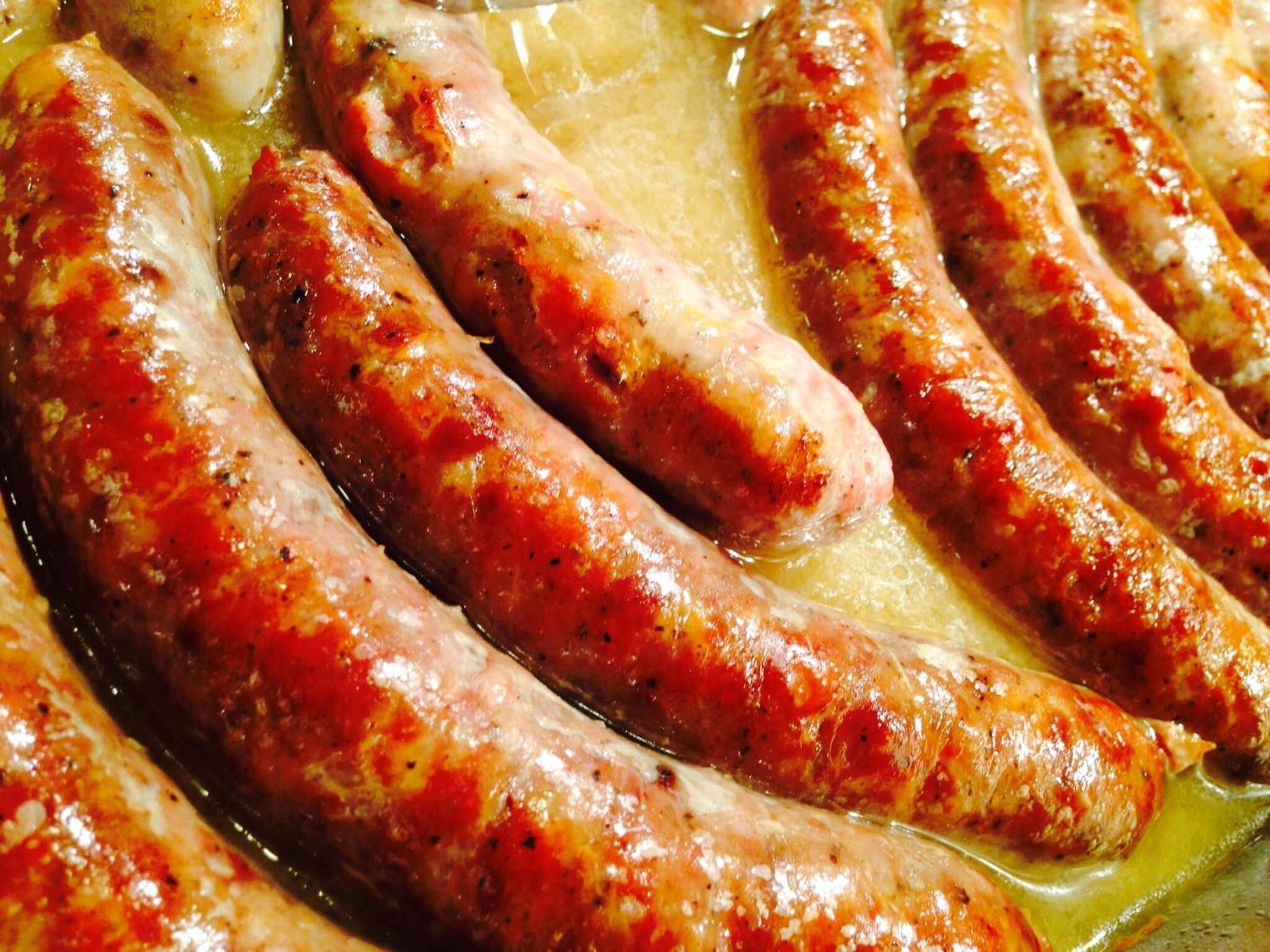 Ein Detailbild von mehreren Würstchen, die in einer Pfanne gebraten werden.