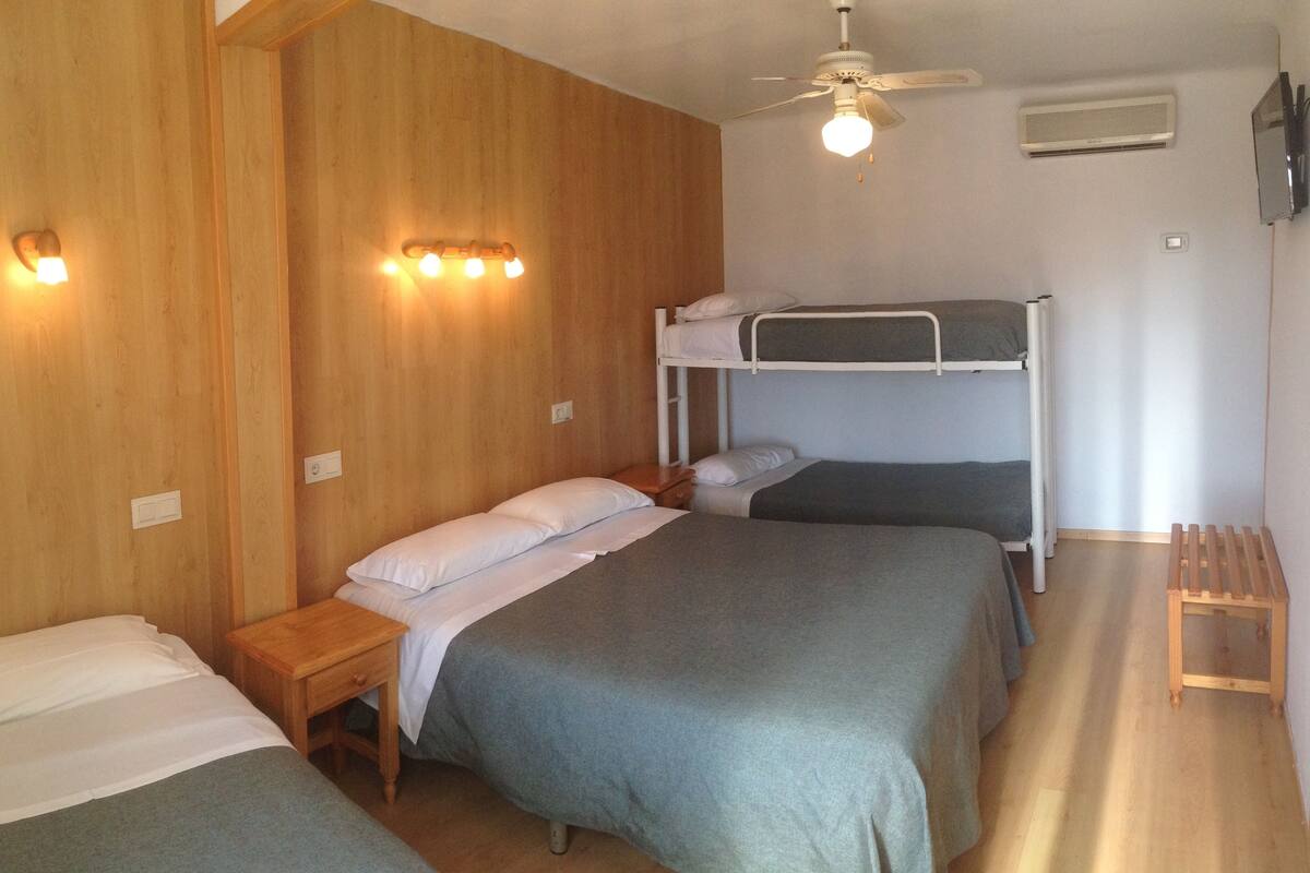Une chambre avec deux lits simples et un lit superposé, des murs en bois, un ventilateur de plafond et des lampes fixées au mur.