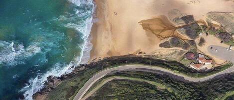 Vista aérea de una zona costera con una carretera serpenteante, playa y edificios dispersos.