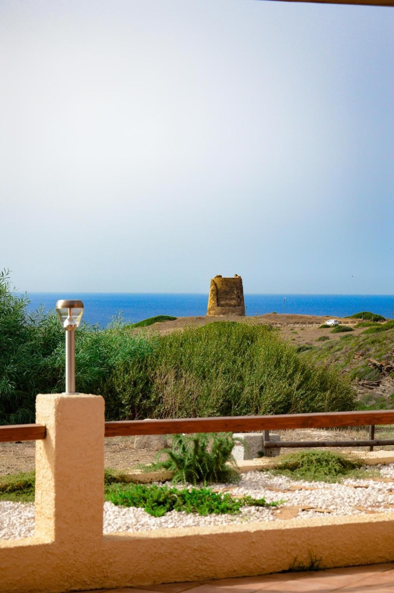 A coastal view with a stone structure in the distance, a railing, and a clear sky.