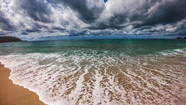 Una spiaggia con acque cristalline e una battigia sabbiosa sotto un cielo nuvoloso.