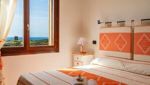Una camera da letto con un letto, un comodino, una lampada e vista mare attraverso una finestra.