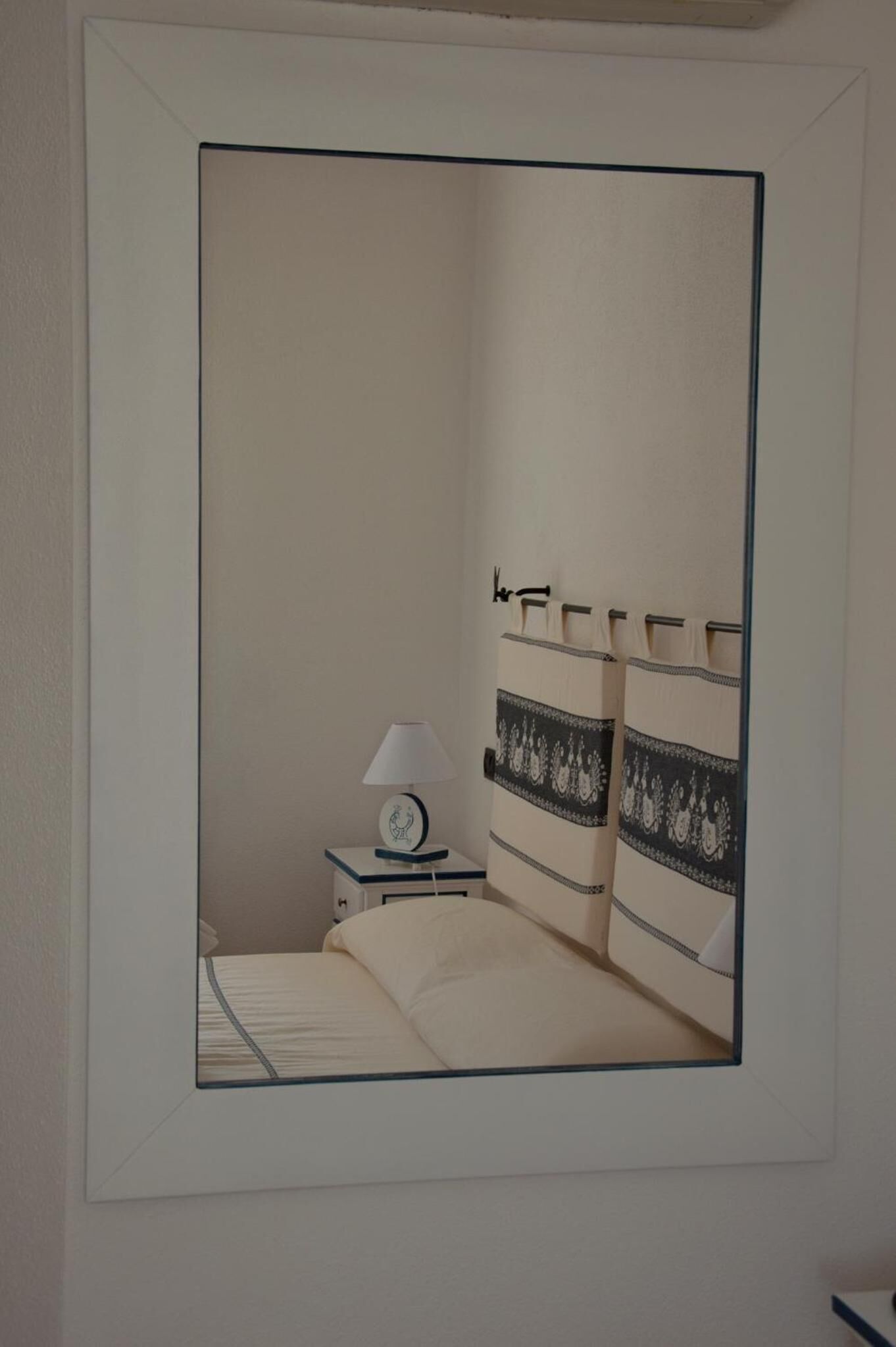 A bedroom with a bed, a nightstand, a lamp, and a mirror.