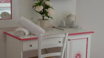 A white desk with a chair, a flat-screen TV mounted on the wall, a vase with flowers, and a small table with cups and a teapot.