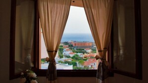 Una stanza con una finestra con tende leggere ripiegate, che mostra una vista di edifici e un corso d'acqua.