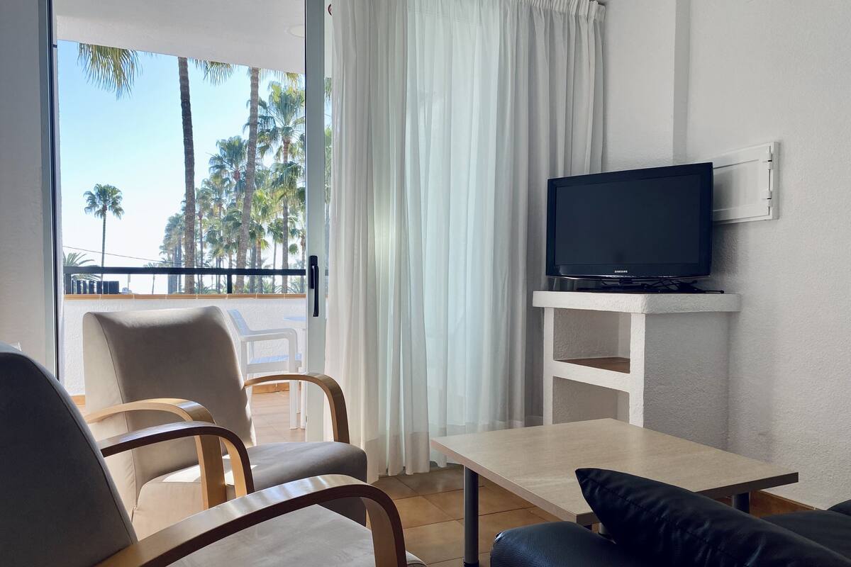 Una sala de estar con una televisión en un estante, un sofá y un sillón.