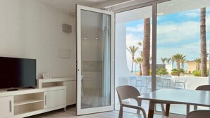 Une chambre moderne dotée d’une télévision, d’une porte-fenêtre coulissante donnant sur un balcon et d’un coin repas avec des chaises.
