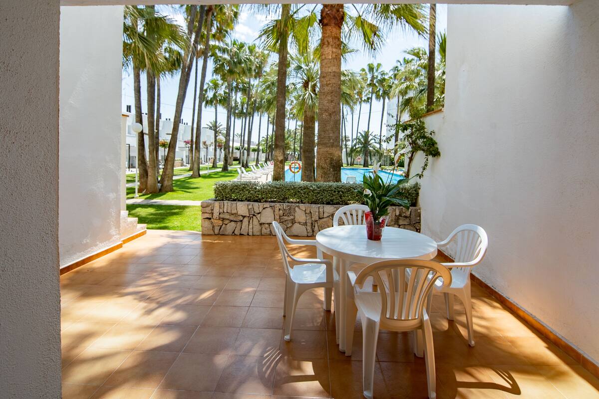 Un patio con una mesa redonda y sillas, un muro de piedra y vistas a palmeras y una piscina.