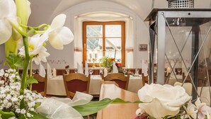 Un coin repas avec des tables dressées pour le repas, une fenêtre avec des rideaux et une lampe en métal sur la droite.
