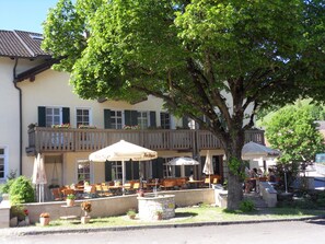 A restaurant with outdoor seating, a stone fountain, and a large tree providing shade. - Hotel Gasthof zum Bräu (Kinding)